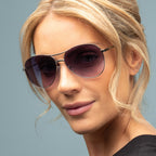 Woman wearing purple sunglasses against a gray background