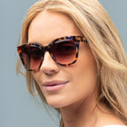 Woman wearing tortoiseshell sunglasses against a gray background