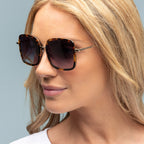 Woman wearing tortoiseshell sunglasses with a neutral background