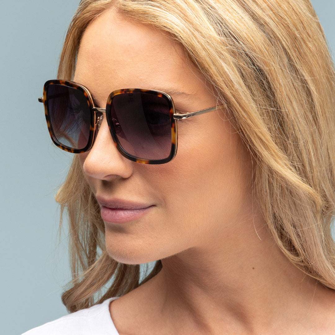 Woman wearing tortoiseshell sunglasses with a neutral background