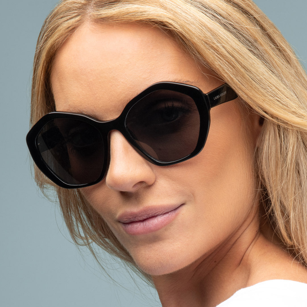 Close-up of a woman wearing black sunglasses against a light gray background