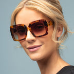 Woman wearing tortoiseshell sunglasses against a light blue background