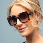 Woman wearing tortoiseshell sunglasses against a light blue background