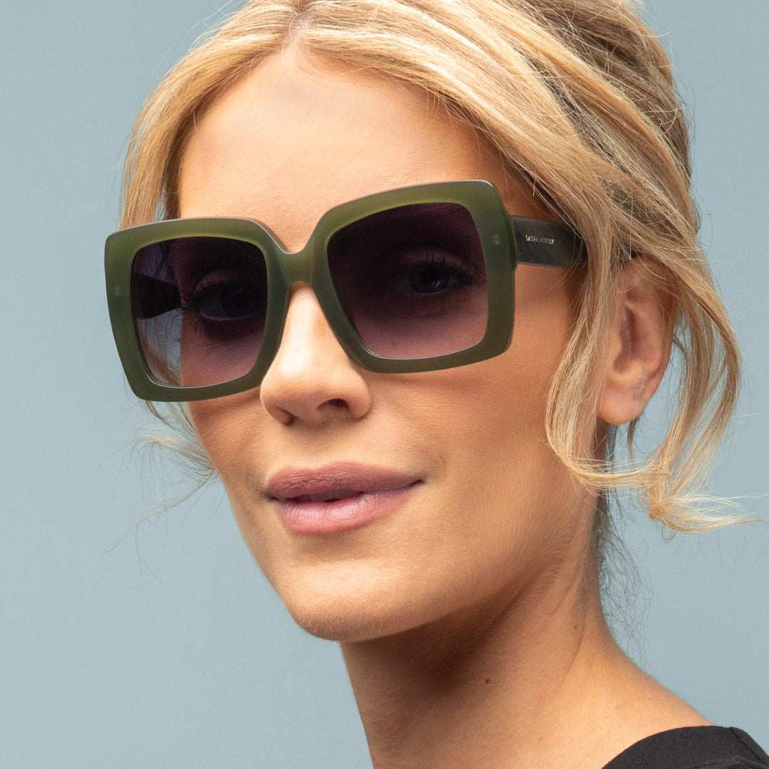 Woman wearing green sunglasses against a light blue background
