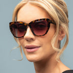 Woman wearing tortoiseshell sunglasses with a neutral background