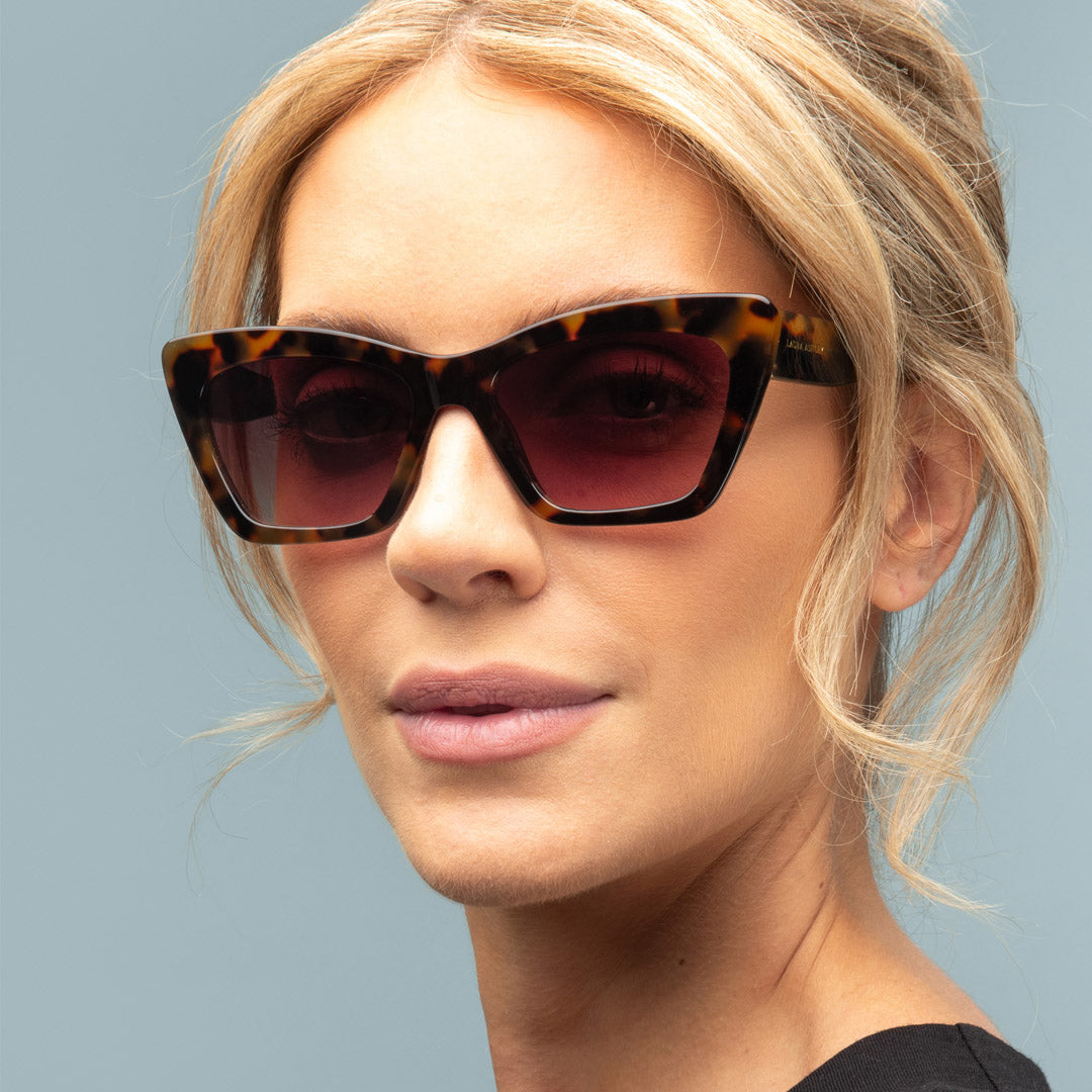 Woman wearing tortoiseshell sunglasses against a light blue background