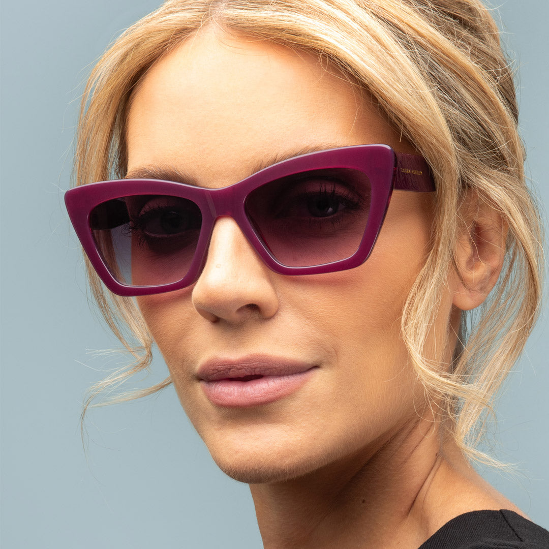 Woman wearing purple sunglasses against a light blue background